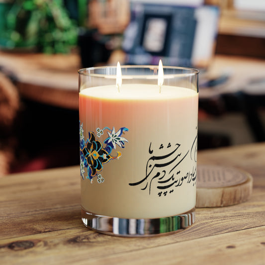 Candle in a glass holder with floral design and Farsi text on a wooden surface.