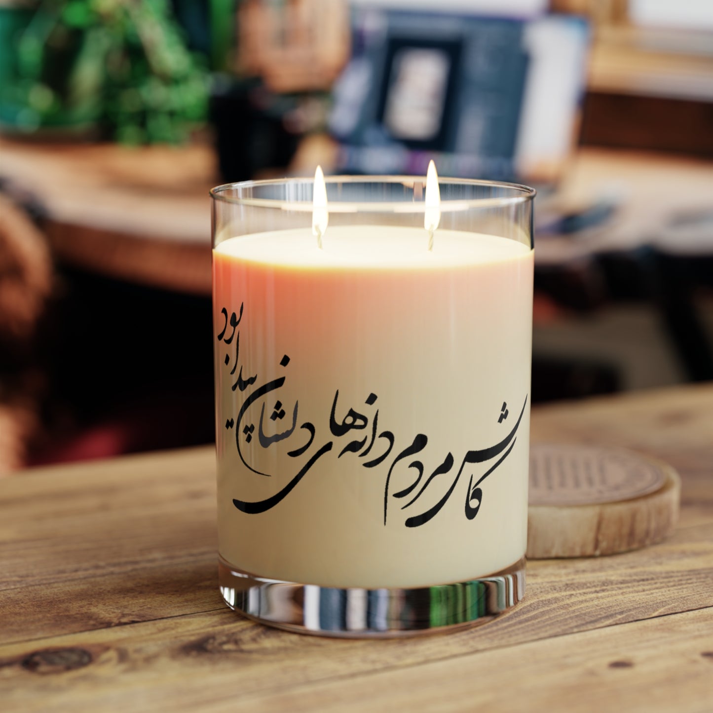 Candle with Farsi calligraphy text in a glass holder on a wooden surface