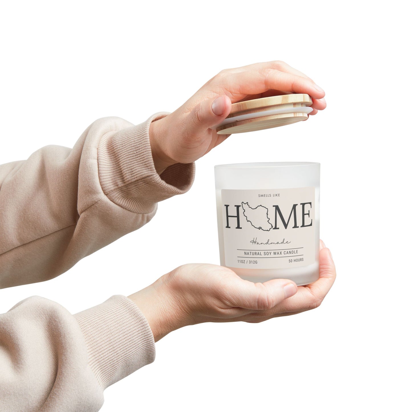 Person holding a 'HOME' candle with a beige sweater sleeve.